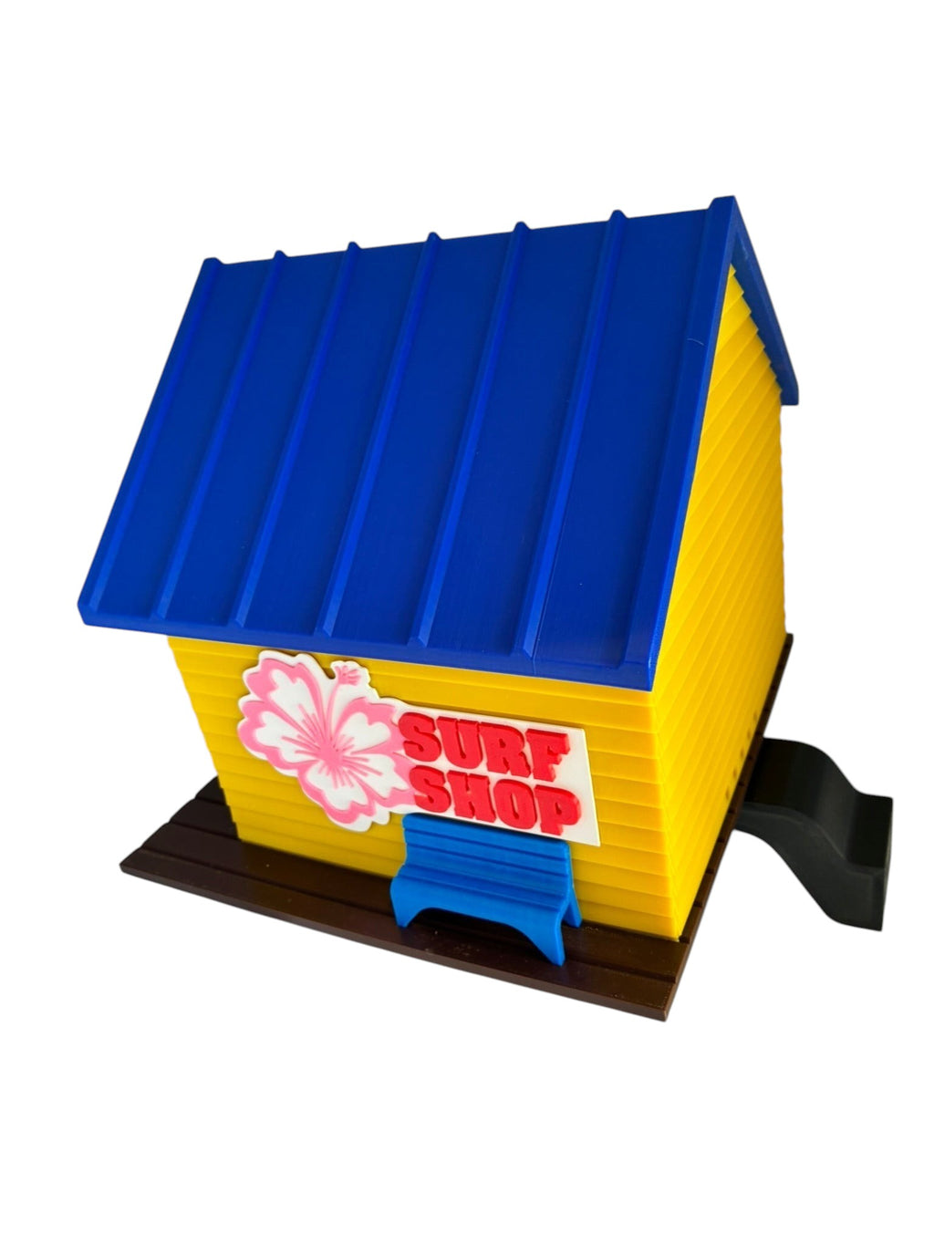 TL3D Prints yellow 3D printed surf shop birdhouse with blue roof, pink hibiscus, and 'SURF SHOP' sign.