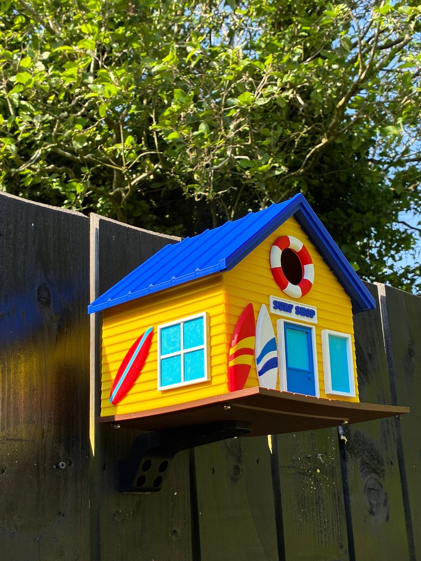 TL3D Prints yellow 3D printed surf shop birdhouse with blue roof, surfboards, and lifebuoy detail.